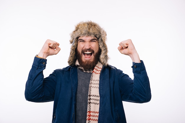 Zdjęcie zdziwiony brodaty mężczyzna ubrany w zimowe ubrania świętuje sukces