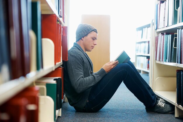 Zdobywanie Materiałów Do Nauki Na Rok Młody Mężczyzna Siedzący Na Podłodze I Czytający W Bibliotece