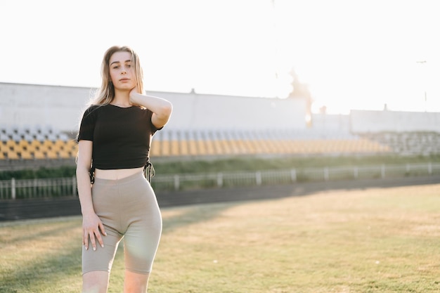 Zdrowa aktywność Blondynka w odzieży sportowej stoi na stadionie Ręka na szyi Sport Lifestyle Concept