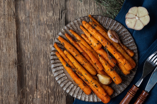 Zdrowa, domowa pieczona marchewka gotowa do spożycia. Glazurowana marchewka z ziołami i czosnkiem. Smażone marchewki na drewnianym tle. Smażone warzywa. Komfortowe jedzenie.