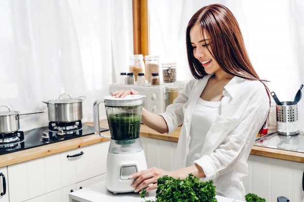 Zdrowa kobieta cieszy się robić zielonemu warzywa detox czyścić i zielonego owocowego smoothie z blender w kuchni w domu dieta pojęcie. zdrowy tryb życia