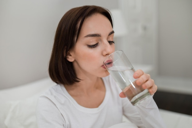 Zdrowa młoda kobieta pijąca świeżą wodę po przebudzeniu zbliżenie