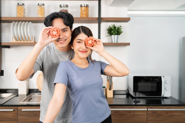 Zdrowa młoda para Azjatów trzymająca w oku świeżego pokrojonego pomidora z uśmiechem i radosnymi emocjami Aktywny styl życia z reklamą zdrowego i wegetariańskiego jedzenia Obraz z miejscem na kopię