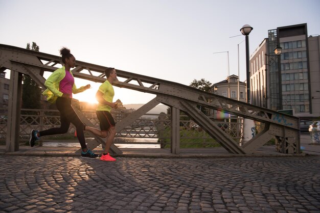 zdrowa młoda wieloetniczna para jogging w mieście wczesnym rankiem ze wschodem słońca w tle