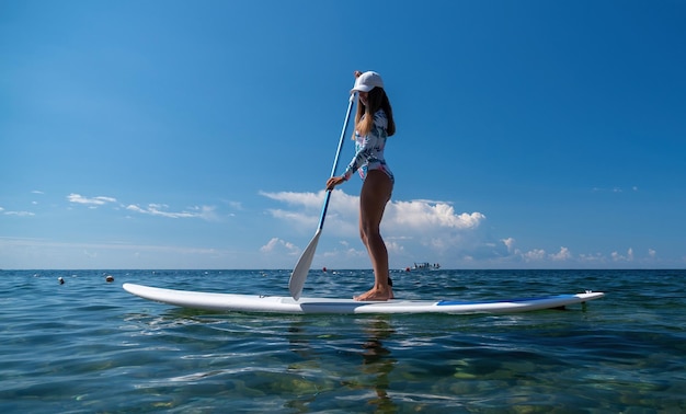 Zdrowa, szczęśliwa sprawna kobieta w bikini relaksuje się na desce surfingowej sup unoszącej się na czystym turkusowym morzu