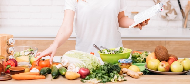 Zdrowa utrata wagi i równowaga żywieniowa. Styl życia kobiety. Kobieta z książką kucharską przygotowuje sałatkę. Asortyment żywności ekologicznej.