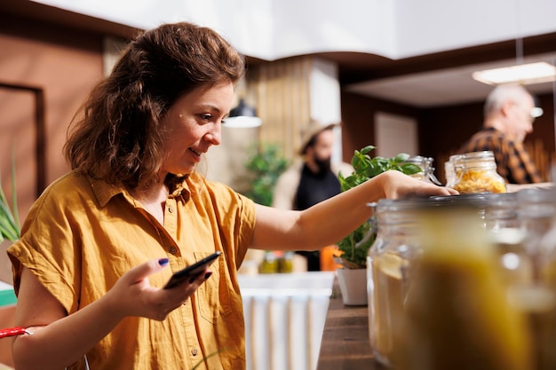 Zdjęcie zdrowa żyjąca kobieta na diecie korzystająca ze smartfona, aby upewnić się, że żywność z supermarketu zero waste jest dla niej odpowiednia. klient w lokalnym sklepie z artykułami biologicznymi upewniający się, że produkty są organiczne