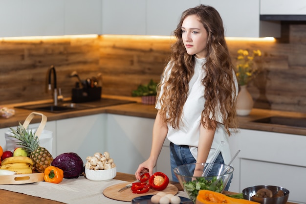 Zdrowa żywność - sałatka jarzynowa. Dieta. Pojęcie diety. Młoda kędzierzawa kobieta przygotowywa jarzynowej sałatki w jej kuchni. Pojęcie zdrowego stylu życia, piękna uśmiechnięta kobieta ciie czerwonego pieprzu dla sałatki.