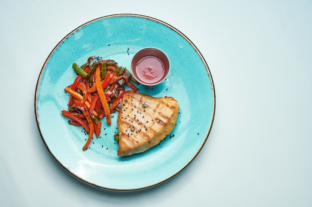 Zdrowe, dietetyczne jedzenie - grillowany filet z indyka z gotowaną marchewką i brokułami w niebieskim ceramicznym talerzu izolowanym jasnoszarą powierzchnią.