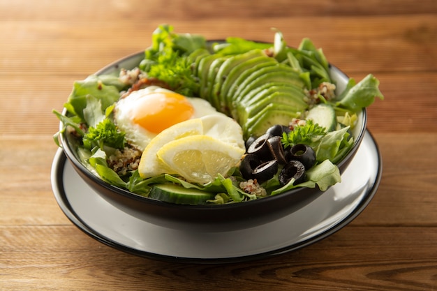 Zdrowe jedzenie. Jajka, komosa ryżowa, awokado, zielona sałatka, czarne oliwki. Drewniany stół. dieta, schudnąć.