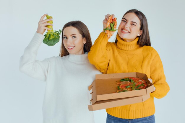 Zdrowe jedzenie. Jedna kobieta trzyma pizzę, a druga brokuły
