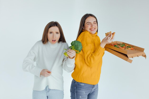 Zdrowe jedzenie. Jedna kobieta trzyma pizzę, a druga brokuły