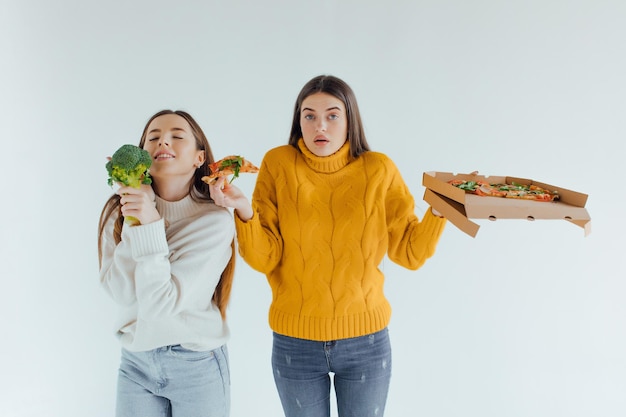 Zdrowe jedzenie. Jedna kobieta trzyma pizzę, a druga brokuły