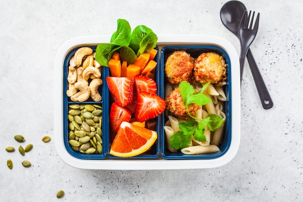 Zdrowe jedzenie lunch box. Wegańska żywność: fasolowe klopsiki, makaron, warzywa, jagody, nasiona i orzechy w pojemniku