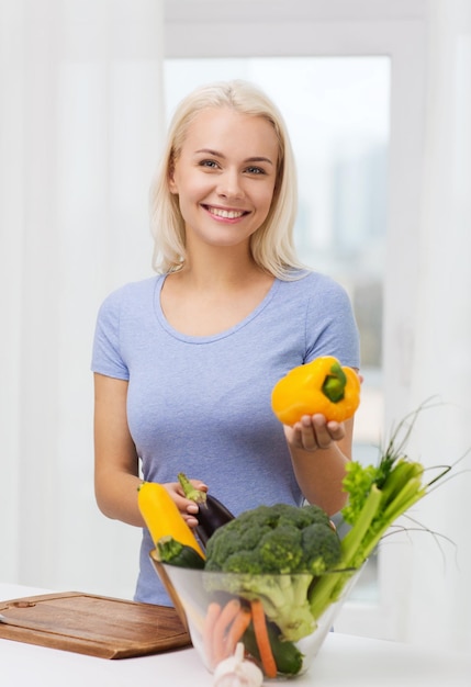 zdrowe odżywianie, gotowanie, wegetariańskie jedzenie, dieta i koncepcja ludzi - uśmiechnięta młoda kobieta z miską warzyw w domu
