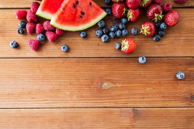 zdrowe odżywianie, jedzenie, dieta i koncepcja wegetariańska - zbliżenie maliny z plasterkami truskawek, jeżyn i arbuza na drewnianym stole