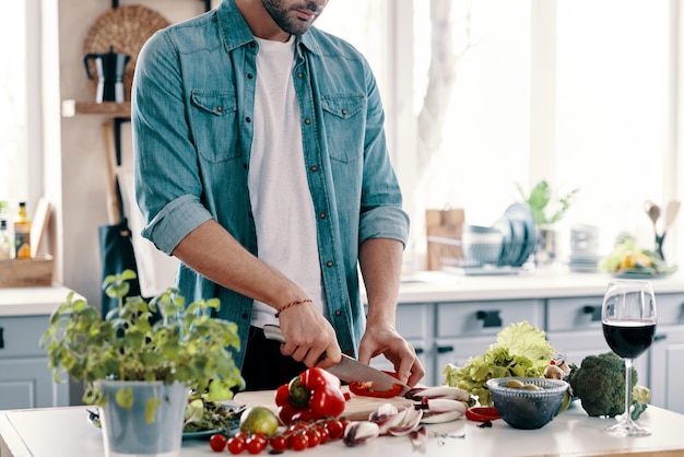 Zdrowe odżywianie. Zbliżenie młodego mężczyzny w stroju casualowym krojenia warzyw, stojąc w kuchni w domu