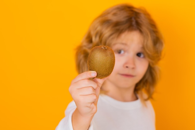 Zdrowe owoce dla dzieci Dziecko trzyma kiwi w studio Owoc kiwi Portret studyjny uroczego chłopca z kiwi odizolowanym na żółto