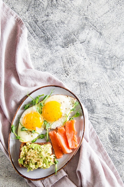 Zdrowe pożywne śniadanie z jajkami, łososiem, kanapką z awokado i kiełkami nasion grochu
