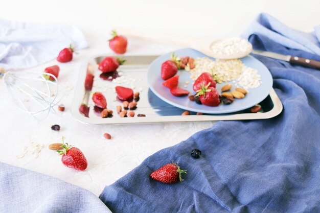 Zdrowe składniki śniadaniowe na stole truskawki, płatki owsiane i orzechy na jasnym tle