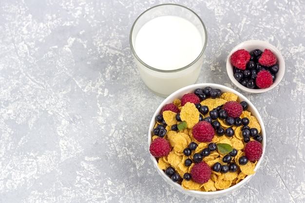 Zdrowe smaczne śniadanie: miska z płatkami kukurydzianymi i jagodami oraz szklanka mleka.