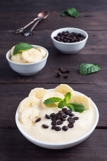 Zdrowe śniadanie, deser z bananem jogurt mleczny i czekoladą na talerzu. Ciemne drewniane.