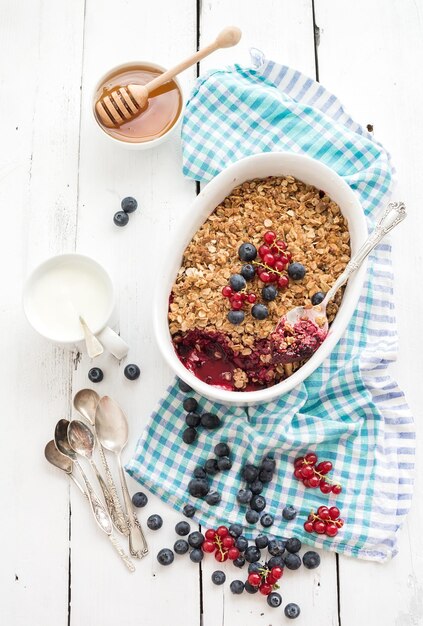 Zdrowe śniadanie Owsiane kruszonka z jagodami muesli z jogurtem ze świeżych jagód i miodem w ceramicznym naczyniu do pieczenia na białym rustykalnym tle