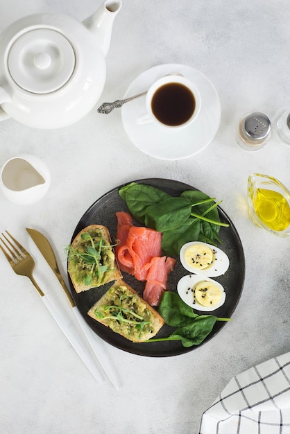 Zdrowe śniadanie z dwiema kanapkami z łososiem z awokado i łososiem w filiżance herbaty na szarym stole
