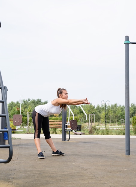 Zdrowy i aktywny tryb życia. Sport i fitness. Szczęśliwa kobieta w białej koszulce ćwiczącej na boisku sportowym w słoneczny letni dzień, rozgrzewka