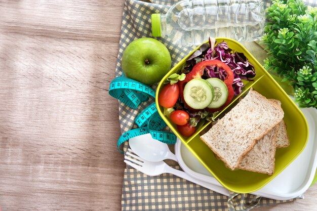 Zdrowy lunchu pudełko z zbożowym chlebem i świeża woda pijemy butelkę na drewnianym tle