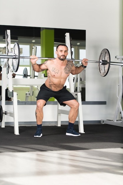 Zdrowy mężczyzna fitness ćwiczący nogi ze sztangą w przysiadach na siłowni