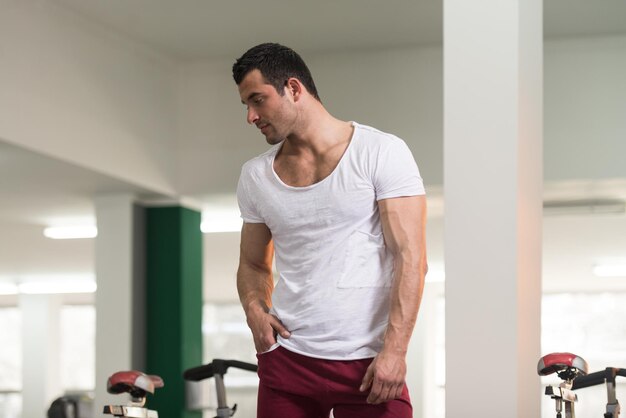 Zdrowy młody człowiek w białej koszulce stojący silny i napinający mięśnie Mięśni atletyczny kulturysta Model fitness pozuje po ćwiczeniach