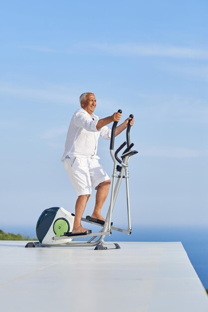 zdrowy starszy mężczyzna ćwiczący na bieżni w siłowni na nowoczesnym tarasie domowym z widokiem na ocean