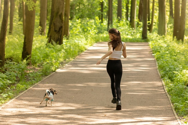 Zdrowy styl życia, zabawa, sport. Dziewczyna biega z psem w parku