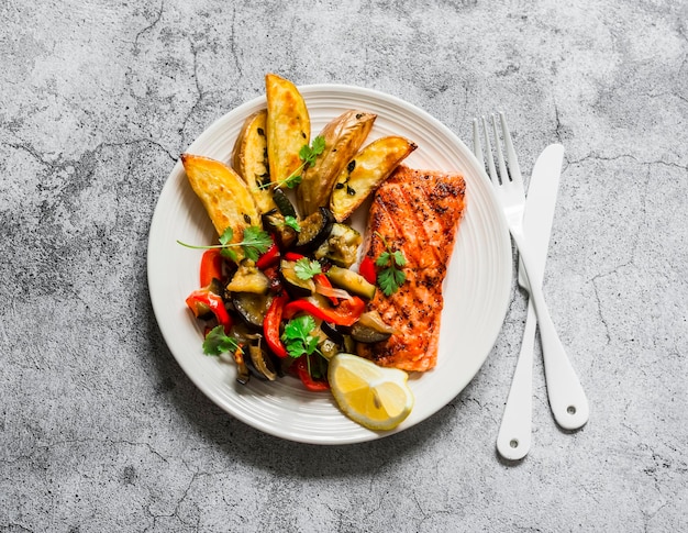 Zdrowy, zrównoważony lunch grillowany łosoś pieczony ratatouille i ziemniaki na szarym tle widok z góry