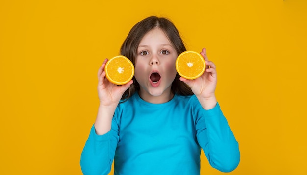 Zdumiewająca nastoletnia dziewczyna trzyma pomarańczową owoc na żółtym tle