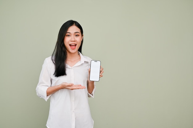 Zdumiona i podekscytowana Azjatka pokazująca makietę smartfona na szarym tle