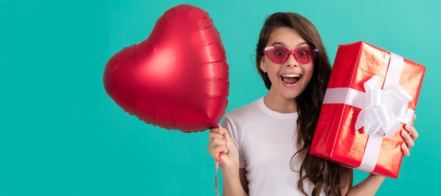 Zdumione dziecko w okularach trzyma pudełko na prezent i przyjęcie walentynkowe serce balon dzień miłości Nastolatka z prezentem urodzinowym poziomy plakat Nagłówek banera z miejsca na kopię