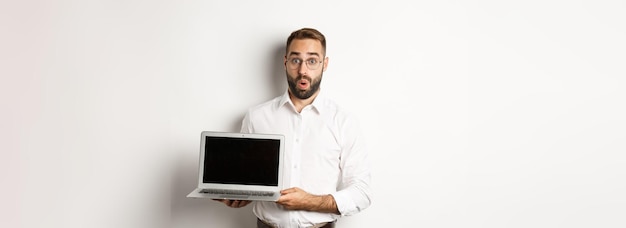 Zdumiony biznesmen pokazujący ekran laptopa stojący na białym tle