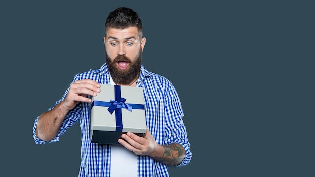 Zdjęcie zdumiony dojrzały brodaty facet z pudełkiem prezentów na szarym tle