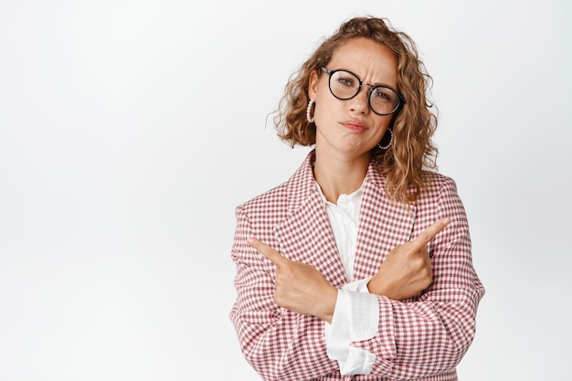 Zdjęcie zdziwiona bizneswoman w okularach dokonuje wyboru, wskazuje na boki w lewo i prawo i marszczy brwi, zaniepokojona wyborem, stoi na białym tle.