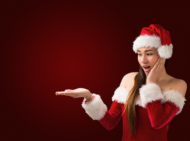 Zdziwiona brunetka przedstawia Santa w stroju z ręką na czerwonym winiety tle