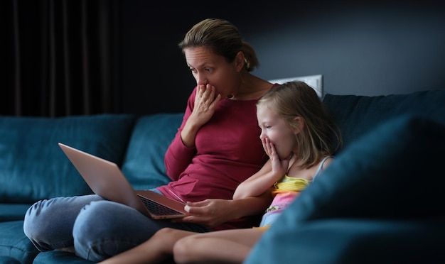 Zdjęcie zdziwiona matka i córka siedzą na kanapie i patrzą na ekran laptopa.