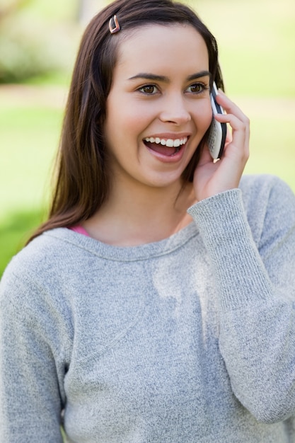 Zdziwiona młoda kobieta opowiada na telefonie podczas gdy stojący w parku