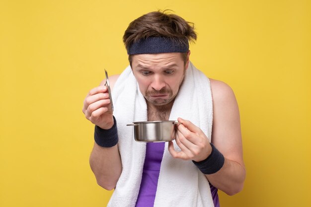Zdjęcie zdziwiony mężczyzna patrzący na jedzenie w małej patelni, zdenerwowany obiadem