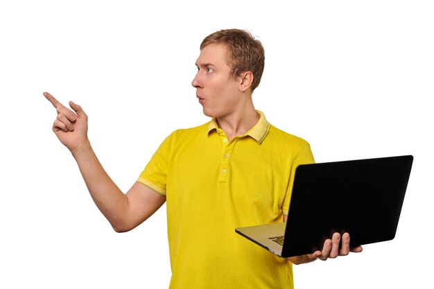Zdziwiony młody człowiek w żółtym Tshort trzymający laptopa w czarnej obudowie i wskazujący palcem na białym tle Zabawny zdezorientowany mężczyzna trzymający notatnik w jednej ręce Zabawny facet z oszołomioną twarzą