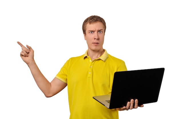 Zdziwiony młody człowiek w żółtym Tshort trzymający laptopa w czarnej obudowie i wskazujący palcem na białym tle Zabawny zdezorientowany mężczyzna trzymający notatnik w jednej ręce Zabawny facet z oszołomioną twarzą