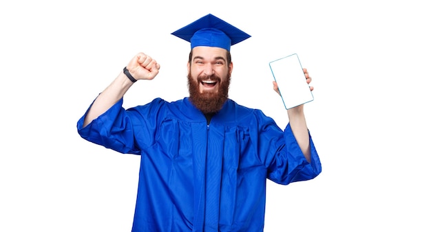 Zdziwiony student człowiek ubrany w niebieską szatę i świętujący trzymając tablet z białym ekranem
