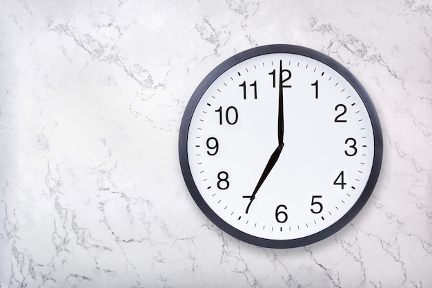 Zegar ścienny pokazuje godzinę siódmą na białej marmurowej fakturze Zegar biurowy pokazuje godzinę 7 wieczorem lub 7 rano