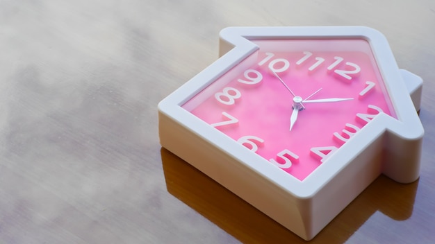 zegar w kolorze różowym i formularz domu na stole roboczym drewna